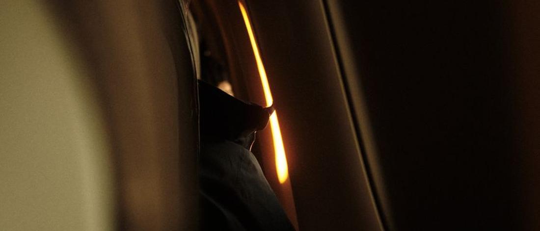 A dimly lit airplane cabin interior with a hint of light from the window, creating a moody ambiance.
