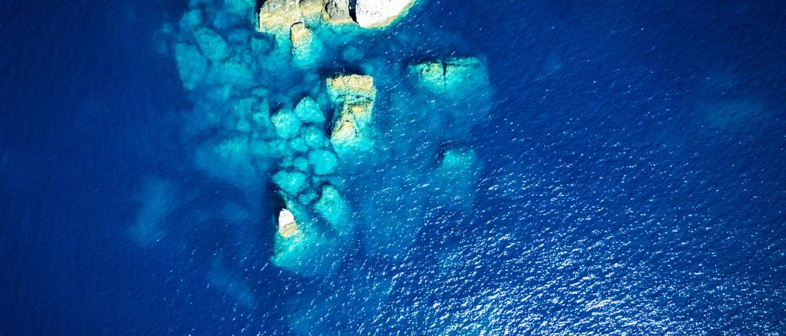 Stunning aerial shot of crystal clear azure waters and rocky formations off the coast of Greece.