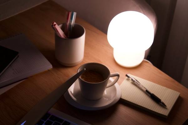 Warm workspace with a glowing lamp and coffee beside a laptop, perfect for late-night work.