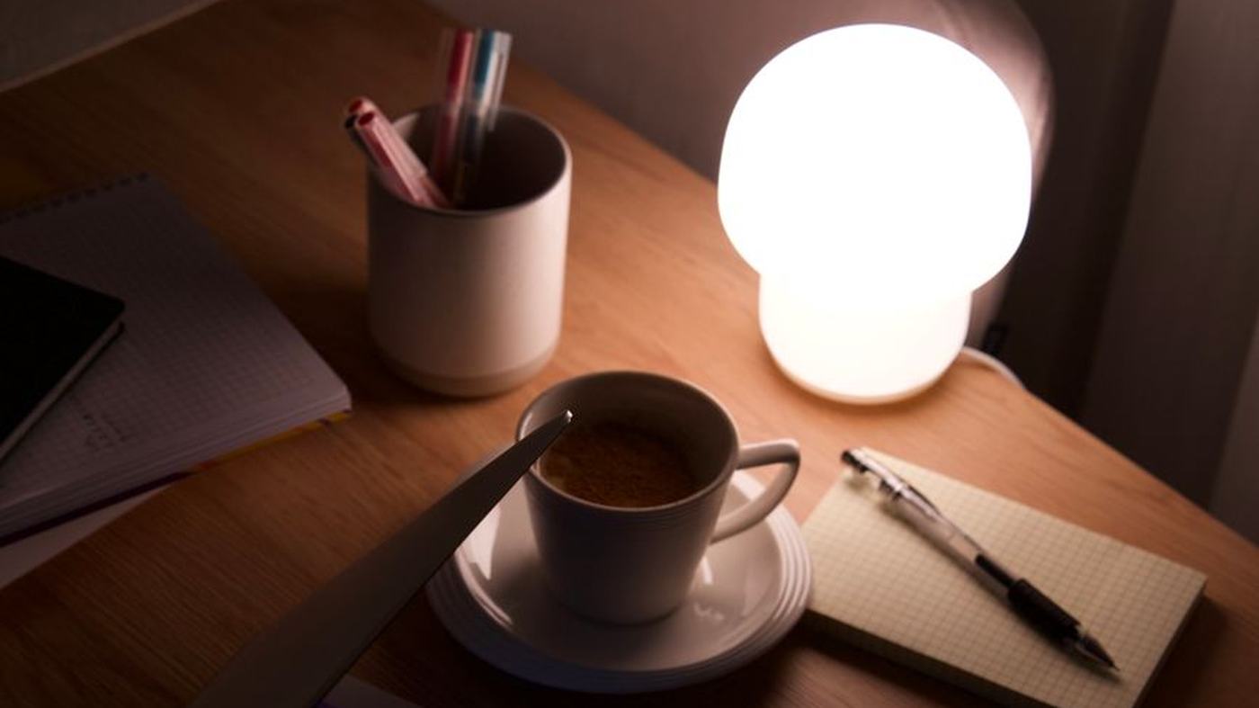 Warm workspace with a glowing lamp and coffee beside a laptop, perfect for late-night work.