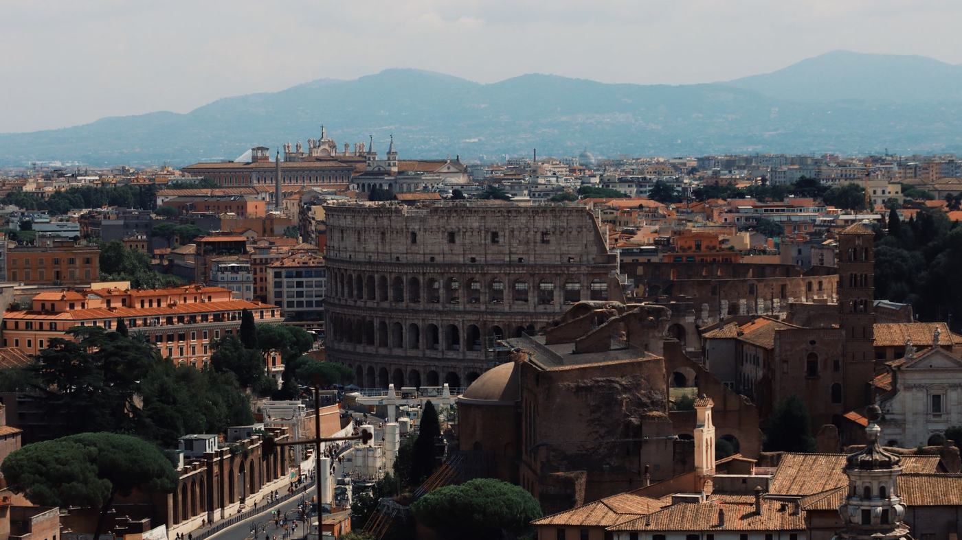 Drone shot of the iconic Colosseum and surrounding cityscape in Rome, Italy.