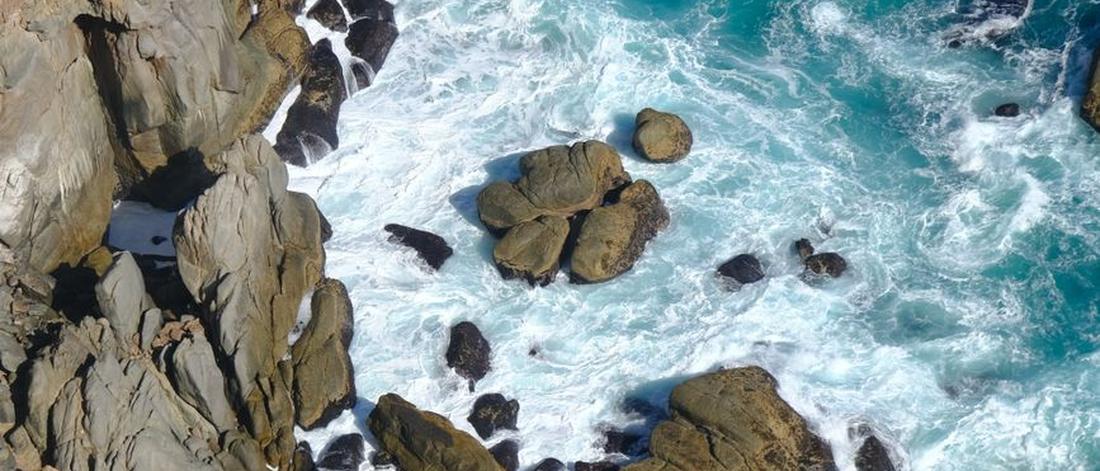 A stunning aerial shot of Cape Town's rocky coastline with crashing waves and vibrant blue waters.