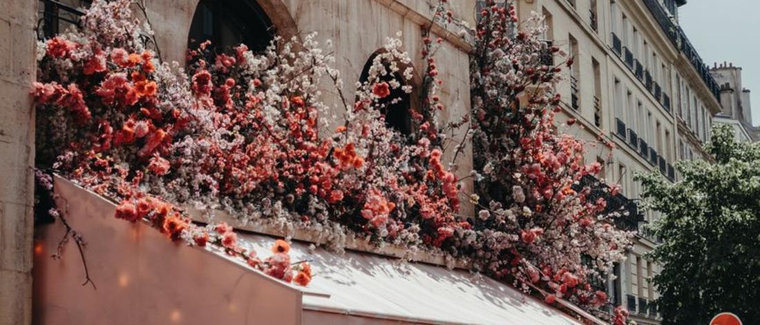 A cozy Parisian café with vibrant floral decorations on a bustling city street.