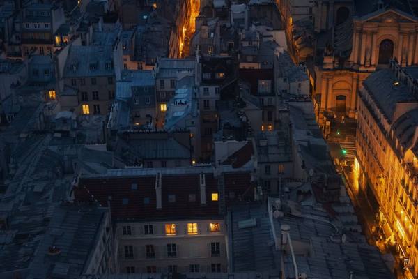 A breathtaking aerial view of Paris rooftops illuminated by warm street lights at night.