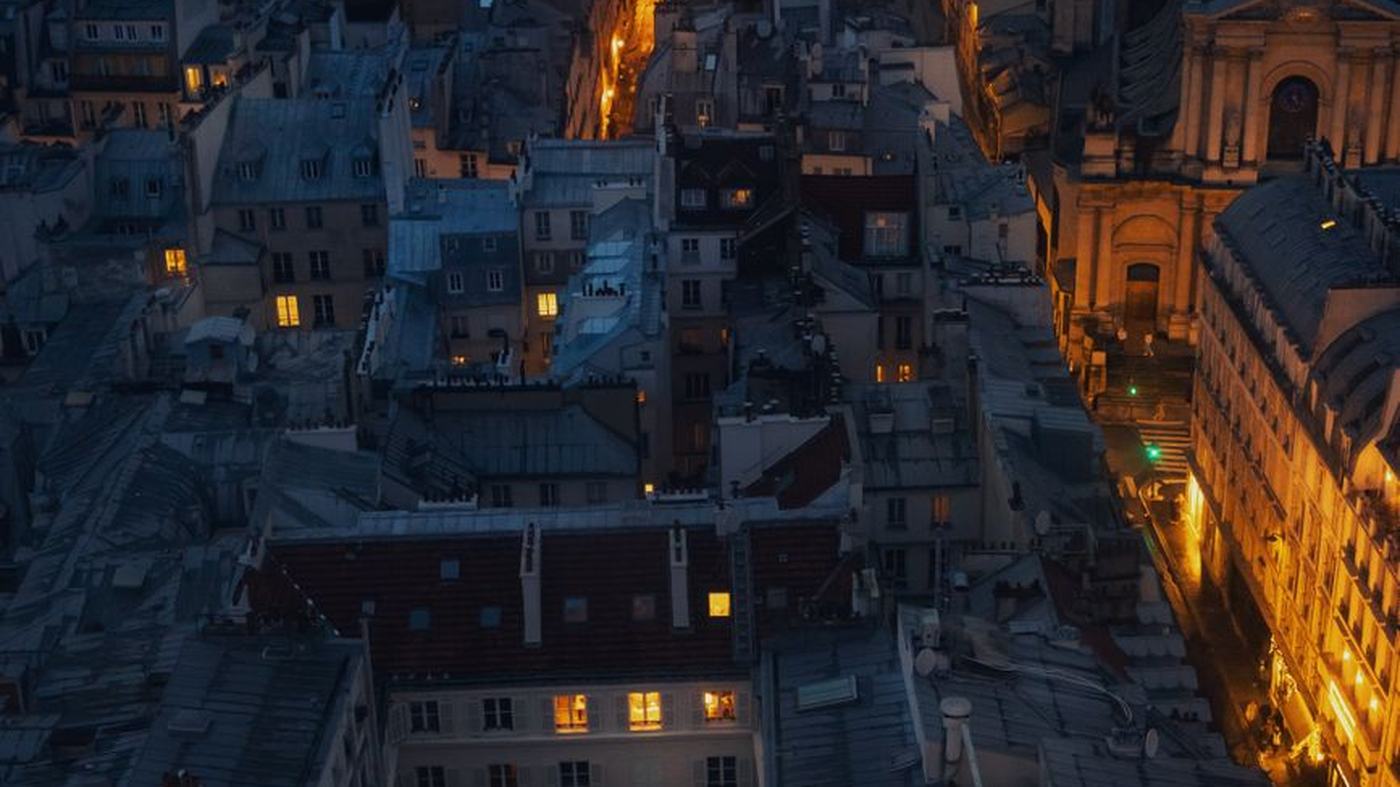 A breathtaking aerial view of Paris rooftops illuminated by warm street lights at night.