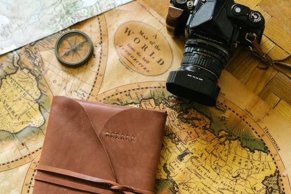 Flat lay of vintage travel items including a map, camera, and leather journal, perfect for wanderlust inspiration.