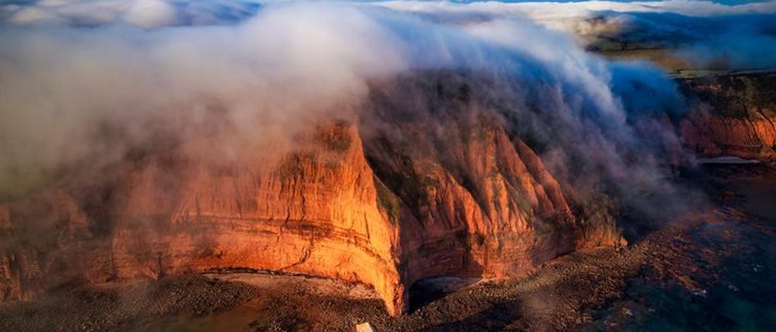 A breathtaking aerial shot of misty cliffs and tranquil water at dawn.