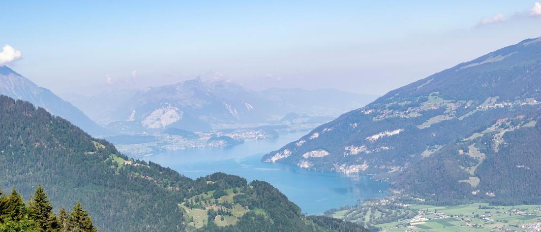 Breathtaking aerial view of Lake Thun surrounded by Swiss Alps mountains with lush greenery and clear blue sky.