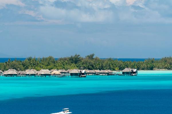 Serene tropical island view with overwater bungalows and a boat cruising by.