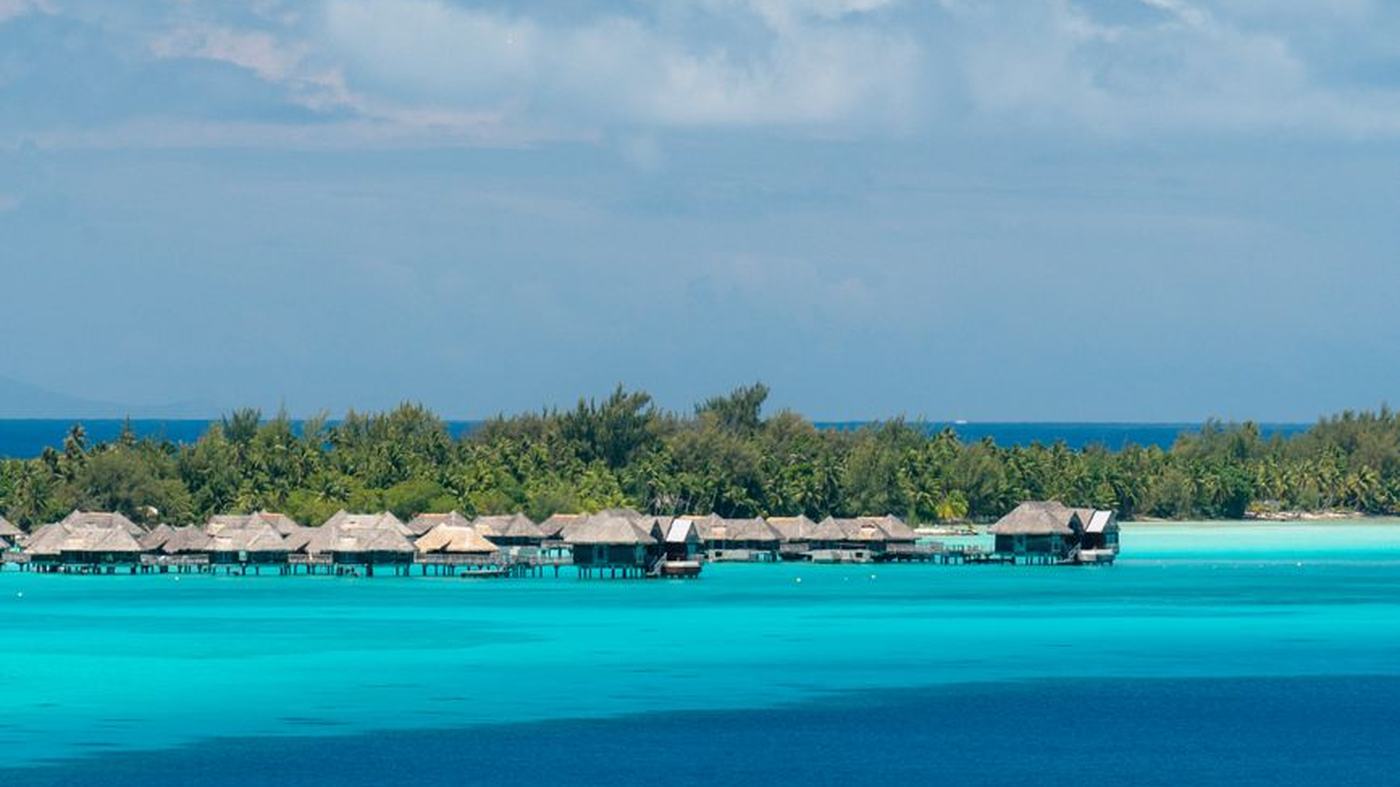 Serene tropical island view with overwater bungalows and a boat cruising by.