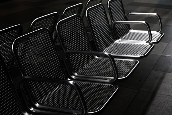 A row of empty metal chairs in a dimly lit terminal, stark and modern.
